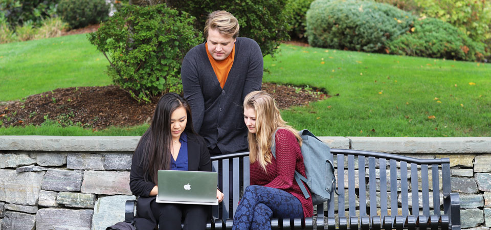 three students on campus looking into laptop