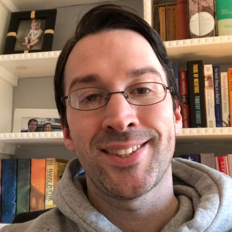 Close up of man smiling with glasses in front of bookcase