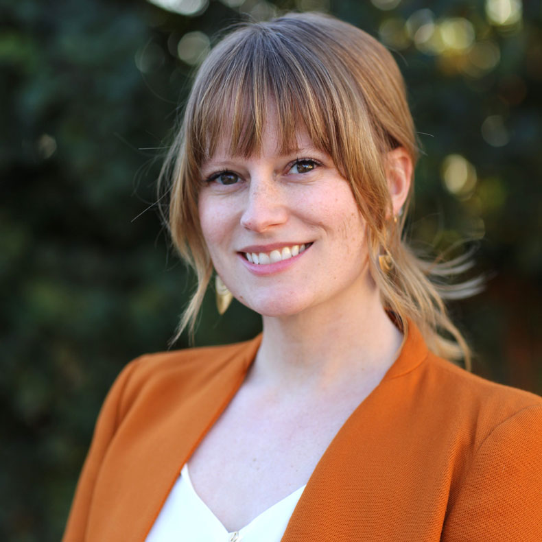 Portrait photo of smiling woman with strawberry blonde hair and orange top