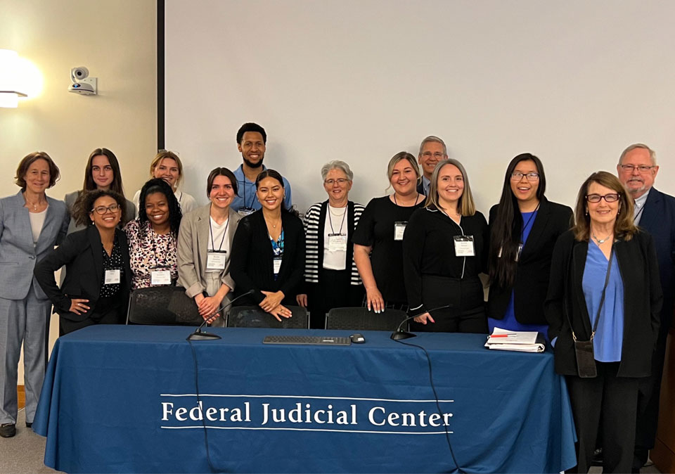 group of men and woman standing in front of table with words Federal Judicial Center banner in front