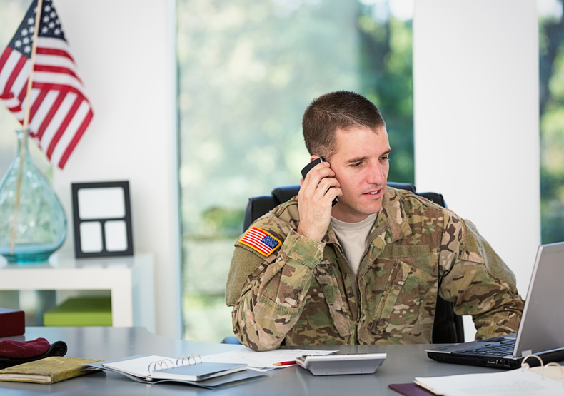 Man in fatigues sitting at desk talking on phone