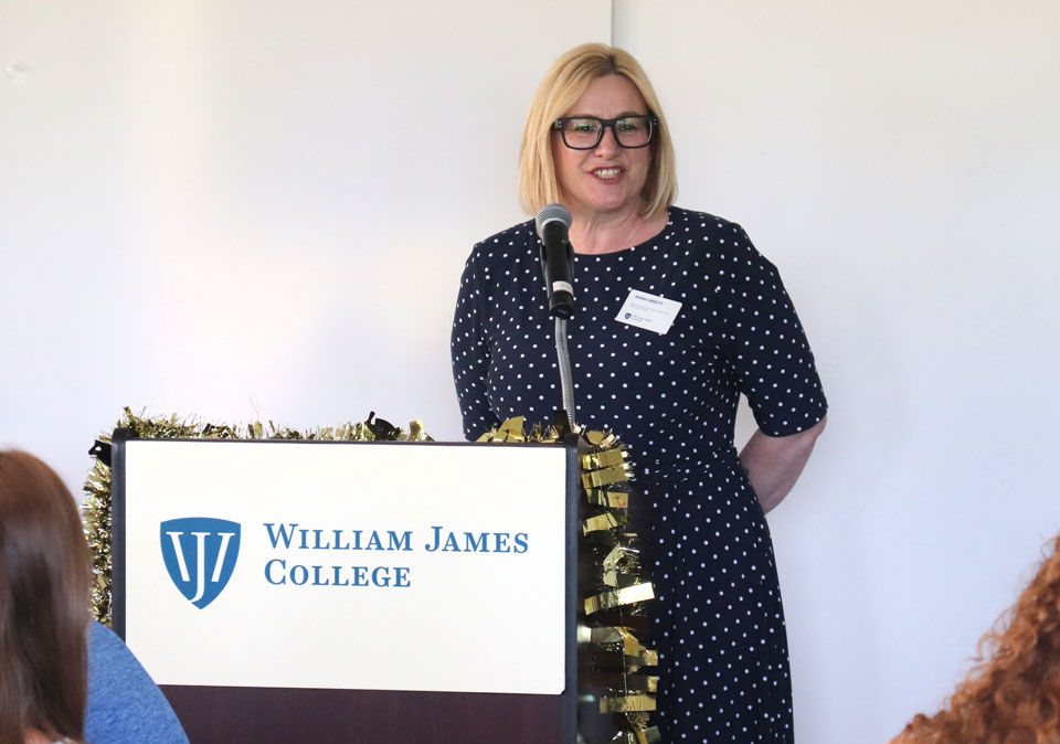 Woman in a dark blue and white polka dot dress standing at a podium smiling