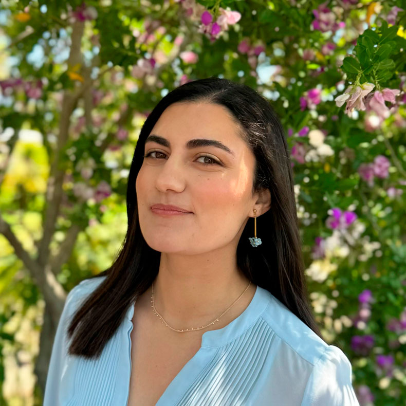 Headshot of smiling woman with dark hair with tree blossoms in background