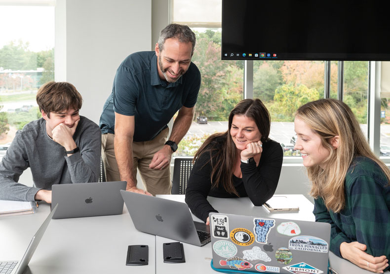 Group of four adults at a table talking with laptops in front of them