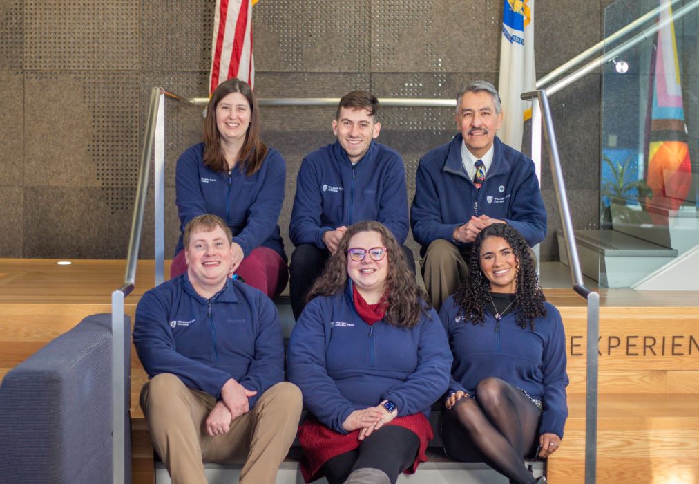 Photo of six admissions staff wearing matching William James College zip up sweaters.