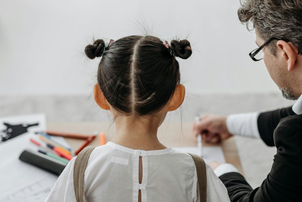 Photo taken from behind of a male adult and young girl student working together at a table