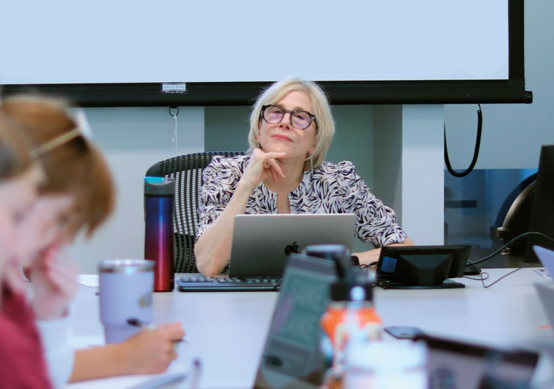 Woman in glasses sitting in front of classroom of students