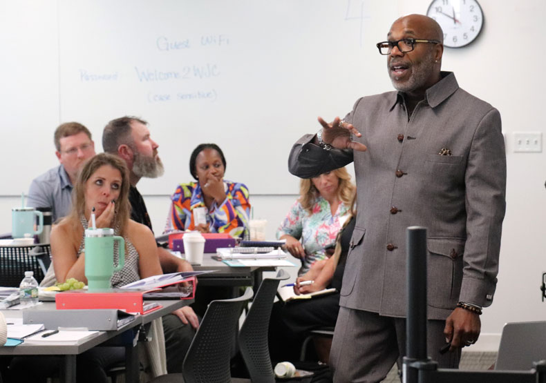 man in gray suit talking with hand gestures in front of classroom of adults