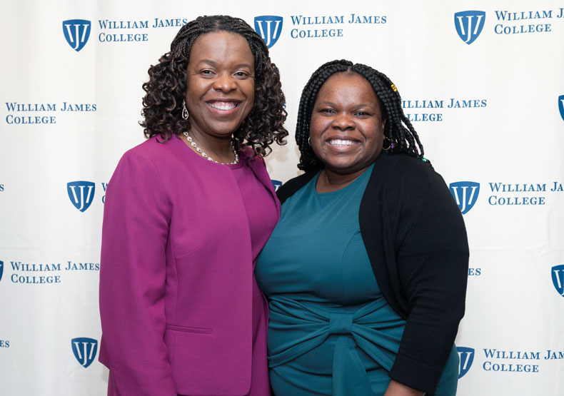 Two women smiling and standing in front of a WJC banner background