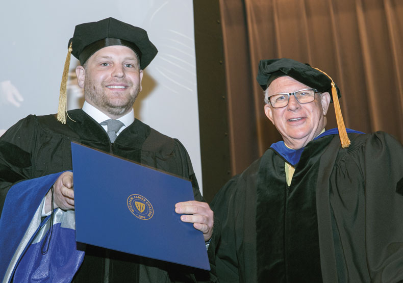 Two men in commencement regalia, one holding a diploma