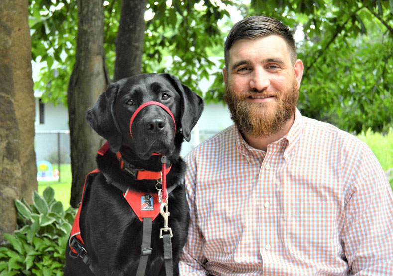 Photo of Kevin Lambert and a black lab, Sally, looking at the camera.