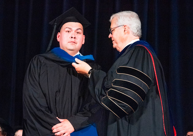 male graduate receiving graduation hood from another male