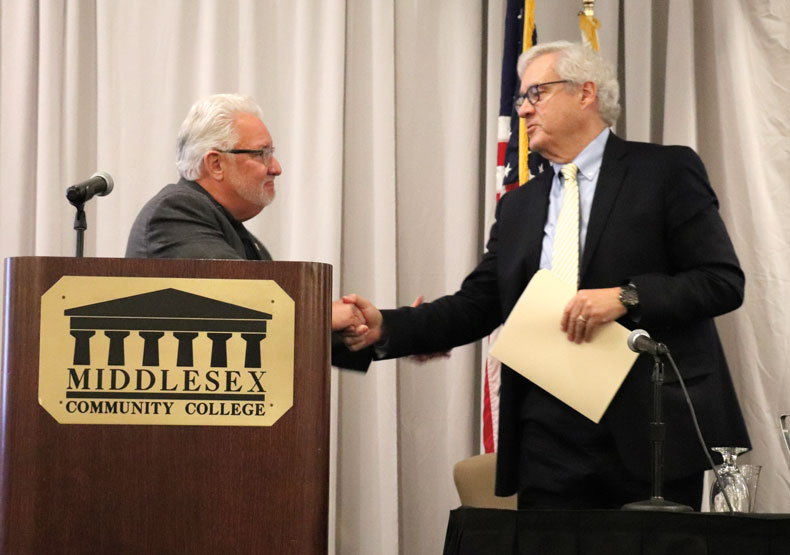 Two men shaking hands in front of podium