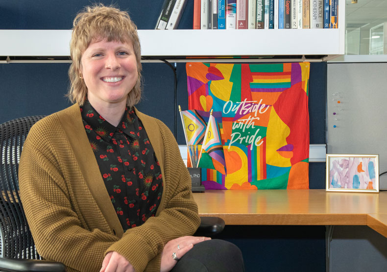 woman smiling sitting at desk with colorful pride banner behind her