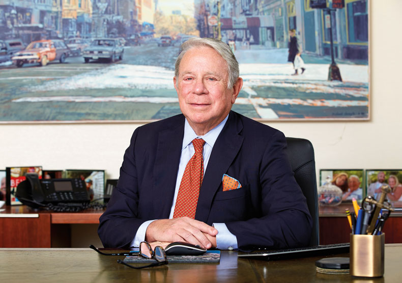 Man sitting at a desk with impressionistic painting of city street scene behind him