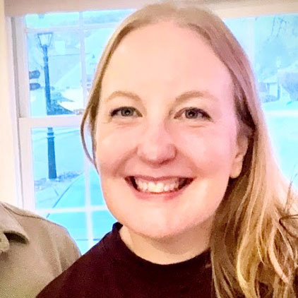 close-up photo of smiling woman with blond hair, with a double hung window behind her